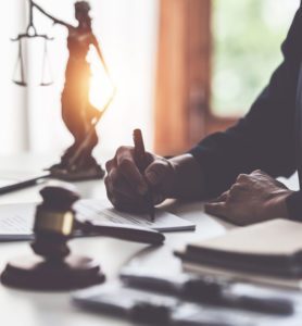 lawyer writing with scales of justice desk figure in background